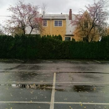 bottom half of the photograph is of a parking lot filled with rain puddles while the top half of the photograph is a yellow house