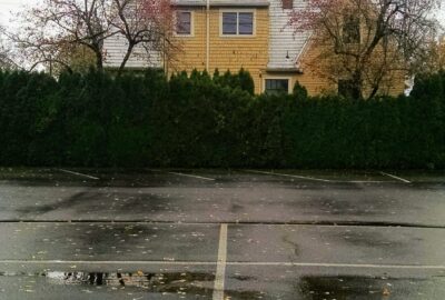 bottom half of the photograph is of a parking lot filled with rain puddles while the top half of the photograph is a yellow house